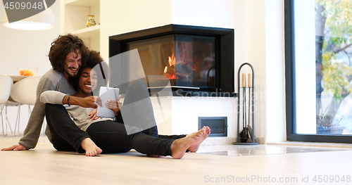Image of multiethnic couple using tablet computer on the floor