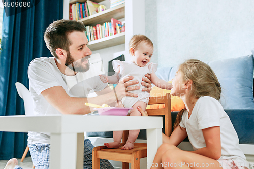 Image of Good looking young man eating breakfast and feeding her baby girl at home