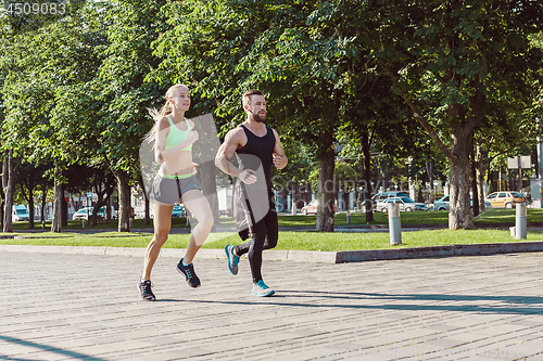 Image of Pretty sporty woman and man jogging at city