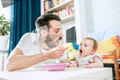 Image of Good looking young man eating breakfast and feeding her baby girl at home