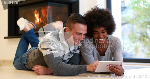 Image of multiethnic couple using tablet computer on the floor