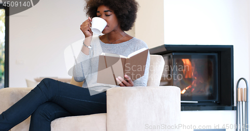 Image of black woman reading book  in front of fireplace