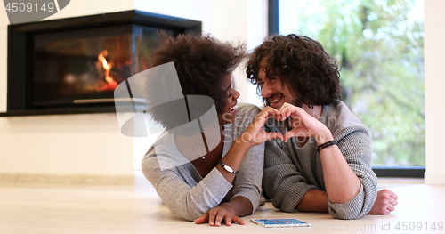 Image of multiethnic couple showing a heart with their hands on the floor