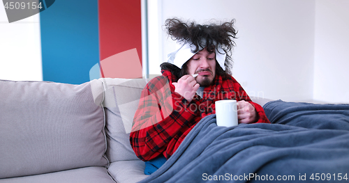 Image of sick man is holding a cup while sitting on couch