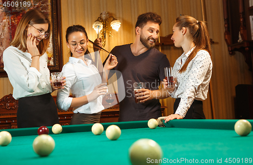 Image of Young men and women playing billiards at office after work.