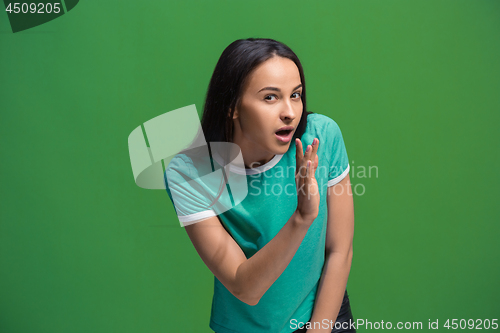 Image of The young woman whispering a secret behind her hand over green background