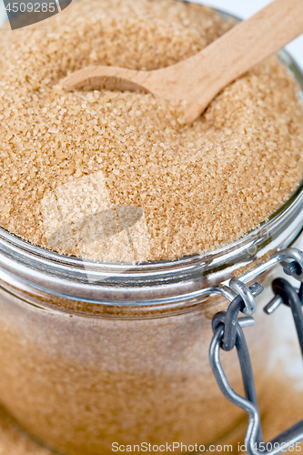 Image of Brown cane sugar in glass jar and wooden spoon closeup image. 