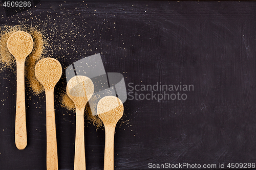 Image of Four wooden spoons with brown cane sugar on black background.