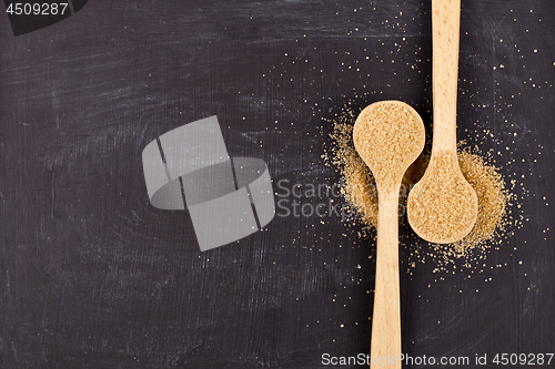 Image of Brown cane sugar in two wooden spoons on black background.