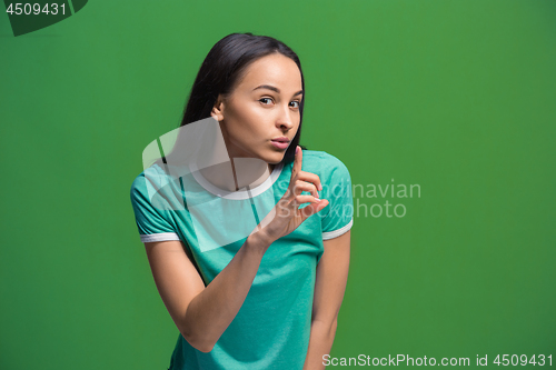 Image of The young woman whispering a secret behind her hand over green background