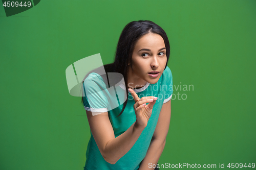 Image of The young woman whispering a secret behind her hand over green background