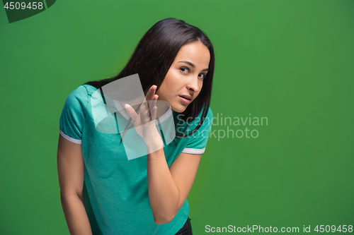 Image of The young woman whispering a secret behind her hand over green background