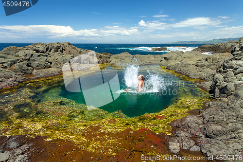 Image of Woman making splash jumping into beautiful rock pool