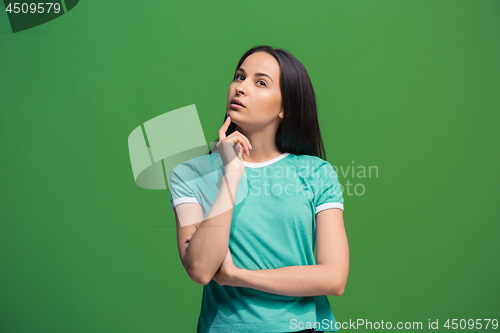 Image of Let me think. Doubtful pensive woman with thoughtful expression making choice against grreen background