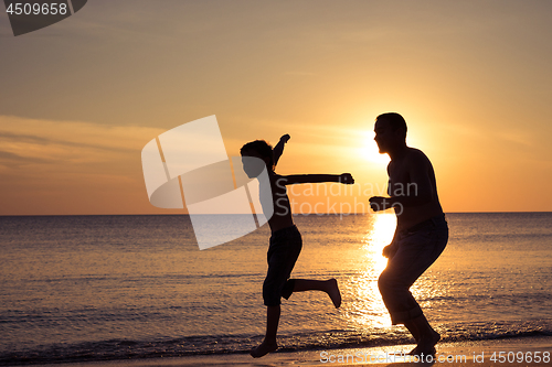 Image of Father and son  playing on the beach at the sunset time.