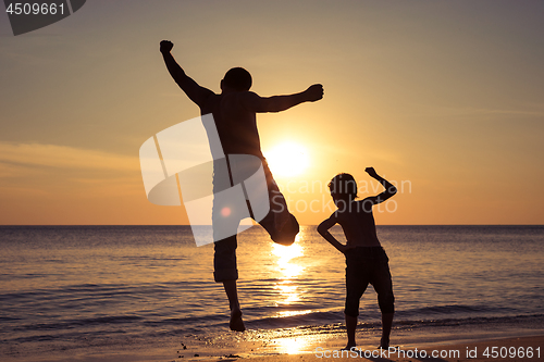 Image of Father and son  playing on the beach at the sunset time.