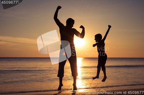 Image of Father and son  playing on the beach at the sunset time.