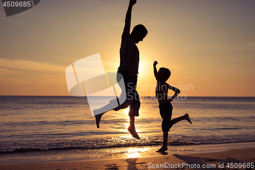 Image of Father and son  playing on the beach at the sunset time.