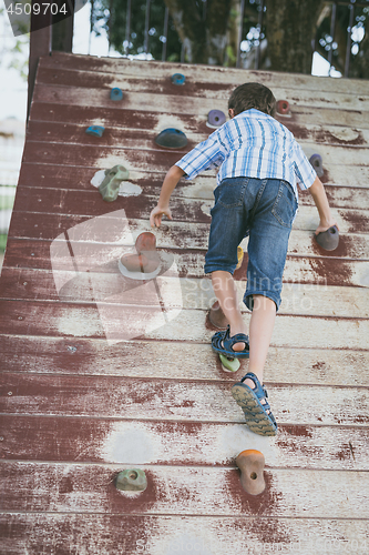 Image of little boy climbing a rock wall outdoor.