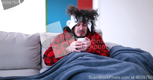 Image of sick man is holding a cup while sitting on couch