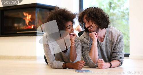 Image of multiethnic couple lying on the floor  in front of fireplace