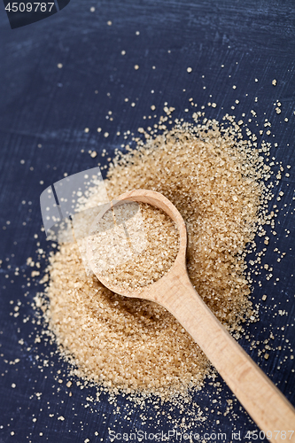 Image of Brown cane sugar in wooden spoon on black board.