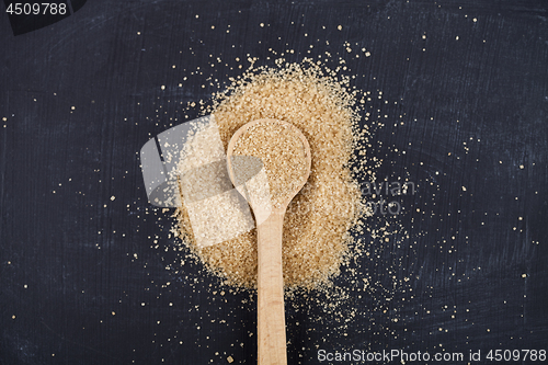 Image of Brown cane sugar in wooden spoon on black board background.