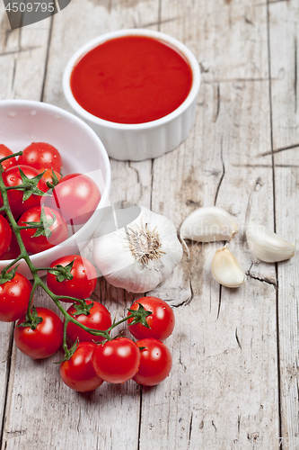 Image of Fresh tomatoes in white bowl, sauce and raw garlic on rustic woo