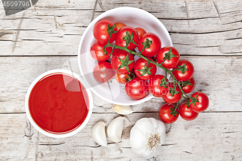 Image of Fresh tomatoes in white bowl, sauce and raw garlic on rustic woo