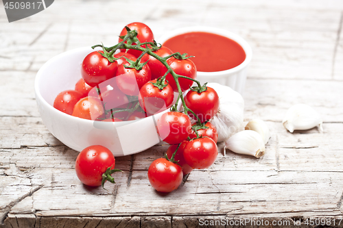 Image of Fresh tomatoes in white bowl, sauce and raw garlic on rustic woo