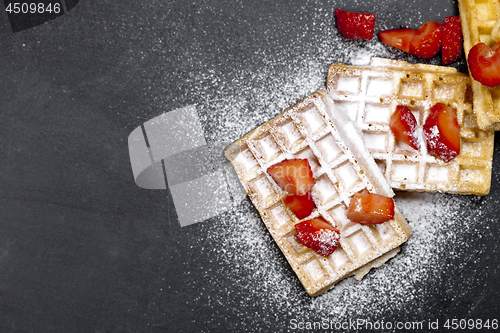 Image of Belgium waffers with strawberries and sugar powder on black boar