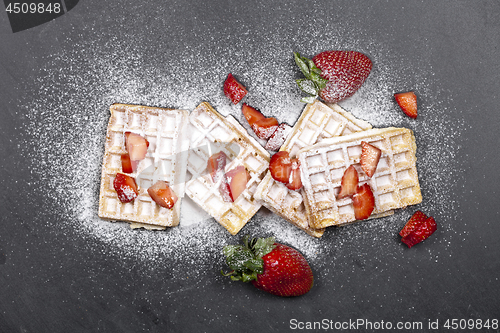 Image of Belgium waffers with strawberries and sugar powder on black boar