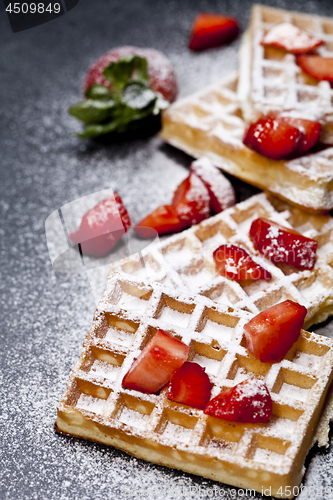 Image of Belgium waffers with strawberries and sugar powder on black boar