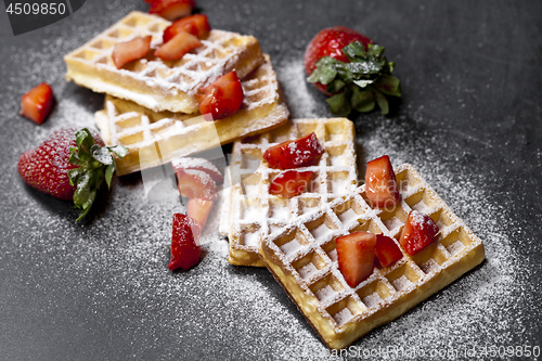 Image of Belgium waffers with strawberries and sugar powder on black boar