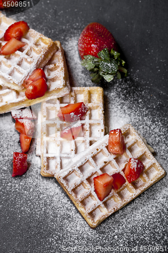 Image of Belgium waffers with strawberries and sugar powder on black boar