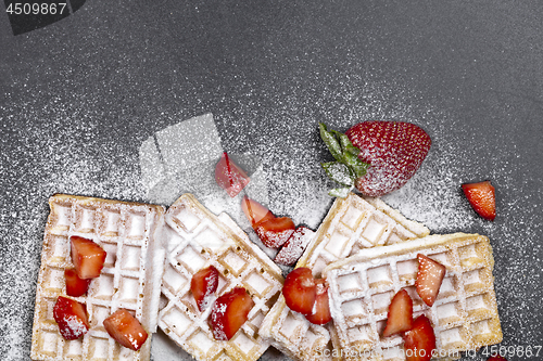 Image of Belgium waffers with strawberries and sugar powder on black boar