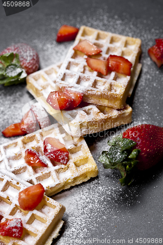 Image of Belgium waffers with strawberries and sugar powder on black boar