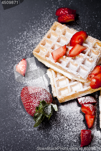 Image of Belgium waffers with strawberries and sugar powder on black boar