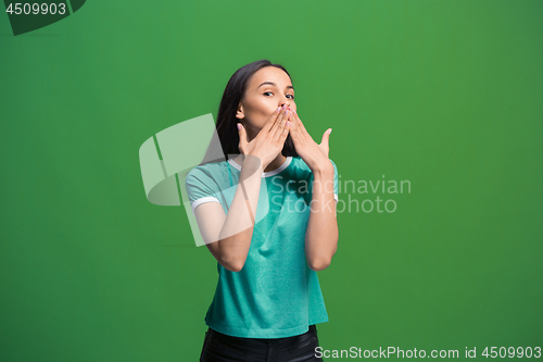 Image of The young woman whispering a secret behind her hand over green background