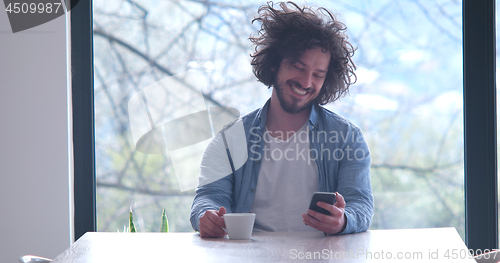 Image of young man drinking coffee and using a mobile phone  at home