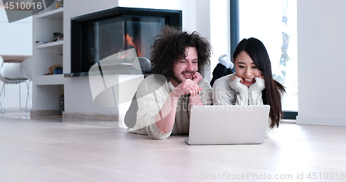 Image of young multiethnic couple using a laptop on the floor