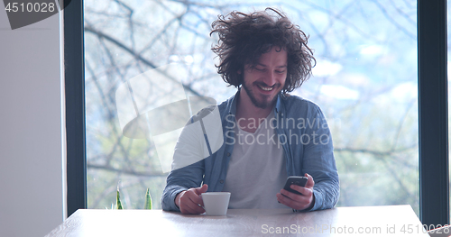 Image of young man drinking coffee and using a mobile phone  at home