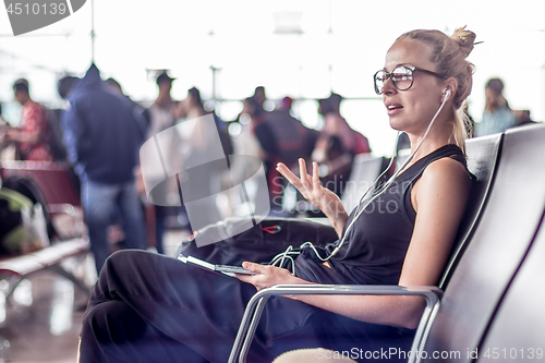 Image of Female traveler talking on cell phone while waiting to board a plane at departure gates at asian airport terminal.