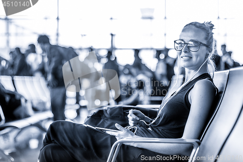 Image of Female traveler using her cell phone while waiting to board a plane at departure gates at asian airport terminal. Blue toned black and white photo.