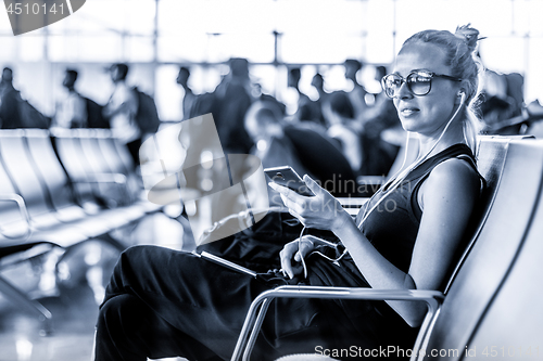 Image of Female traveler using her cell phone while waiting to board a plane at departure gates at asian airport terminal. Blue toned black and white photo.