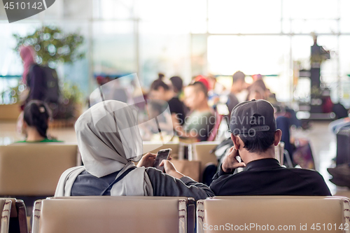 Image of Modern muslim islamic asian couple using their smartphone apps while sitting and waiting for flight departure at international airport terminal