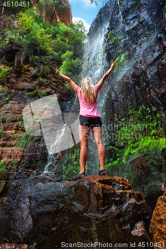 Image of Woman stands on rock in front of cascading waterfall