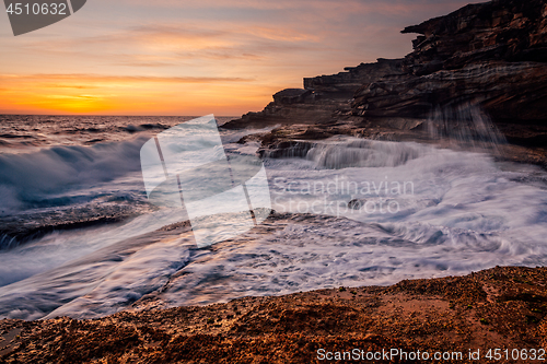 Image of Sunrise and ocean cascades along coastal rocks and headland