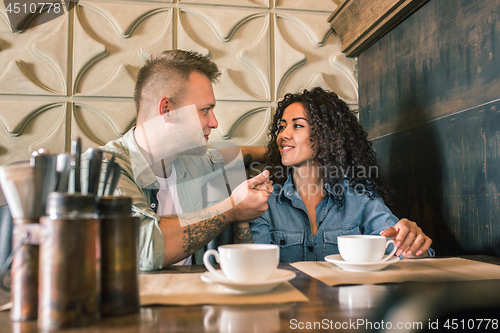 Image of Happy young couple is drinking coffee and smiling while sitting at the cafe