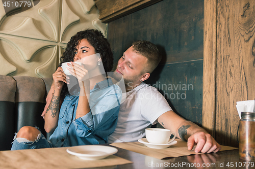 Image of Happy young couple is drinking coffee and smiling while sitting at the cafe